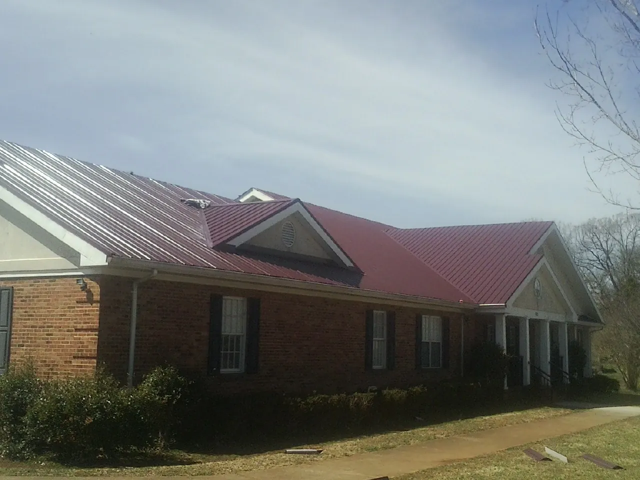Red metal roof with gabled entries on a long brick building, from a Hail Damage Roof Repair job in Somers Point