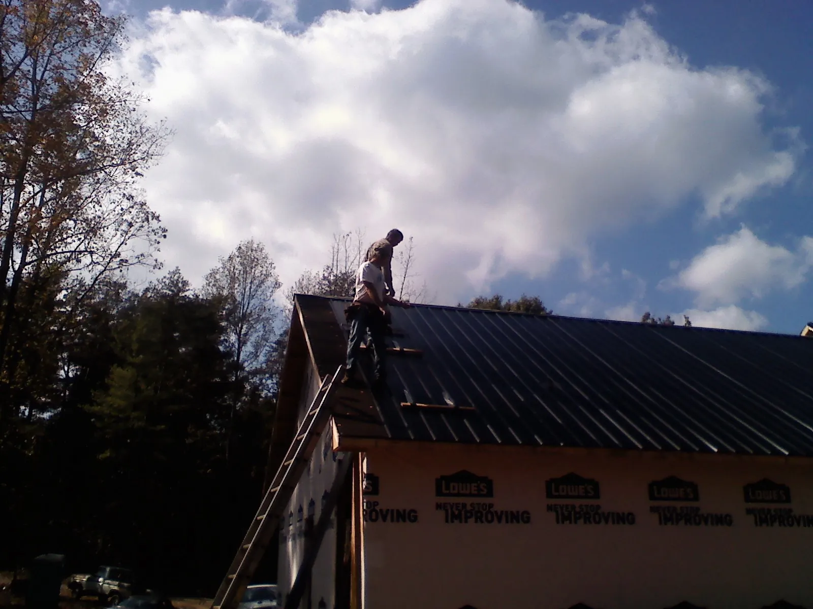Roofer fastening dark metal panels high against a cloudy sky, from a Roof Inspection job in Somers Point