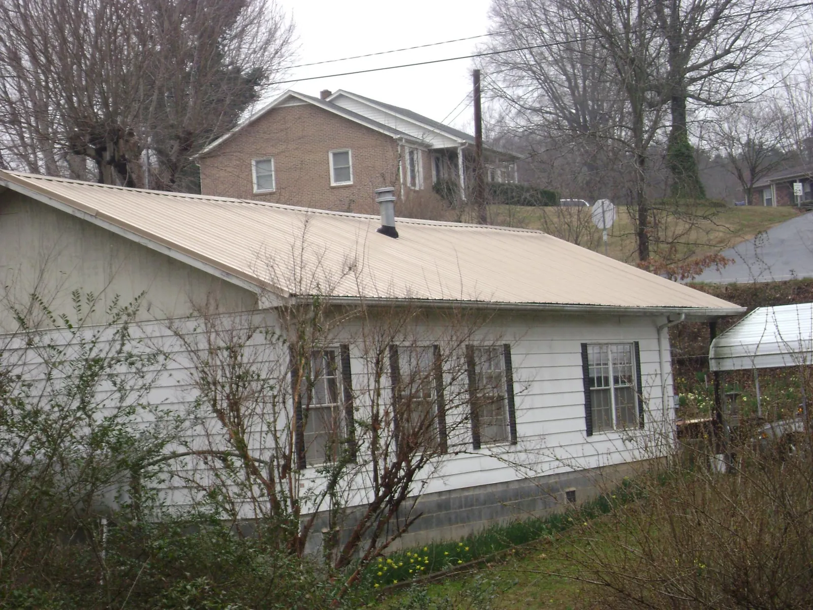 Tan metal roof on a white sided house set into a hillside — Commercial Roofing by Roofing Brothers in Somers Point